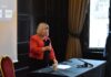 MP Backs the Biggest Mental Health Redesign in a Generation Liz Twist MP standing and speaking into a handheld microphone at an event, wearing a red jacket, beside a table