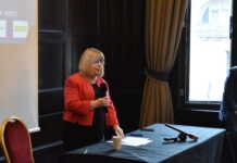 MP Backs the Biggest Mental Health Redesign in a Generation Liz Twist MP standing and speaking into a handheld microphone at an event, wearing a red jacket, beside a table