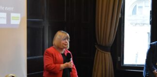 MP Backs the Biggest Mental Health Redesign in a Generation Liz Twist MP standing and speaking into a handheld microphone at an event, wearing a red jacket, beside a table